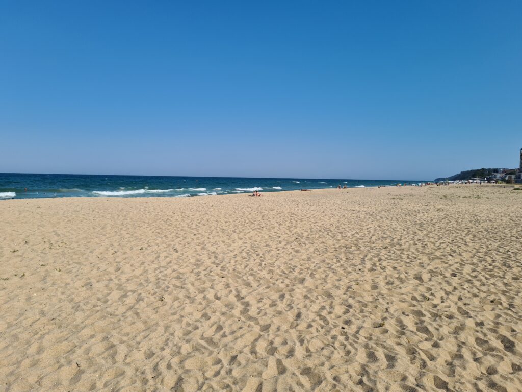 Plajă întinsă cu nisip și mare sub cer senin