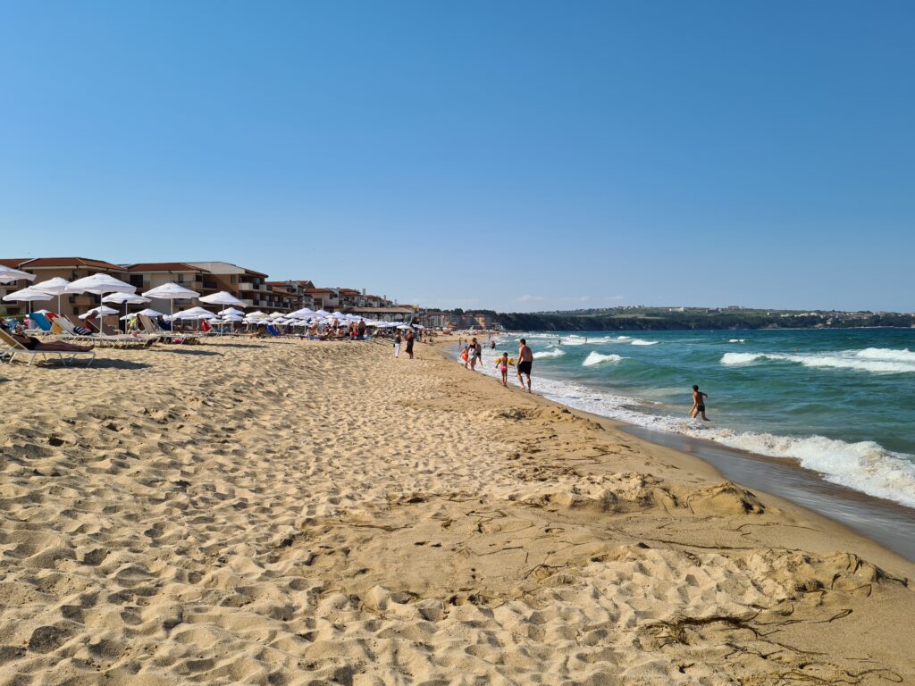 Plajă cu umbrele, turiști și valuri la mal