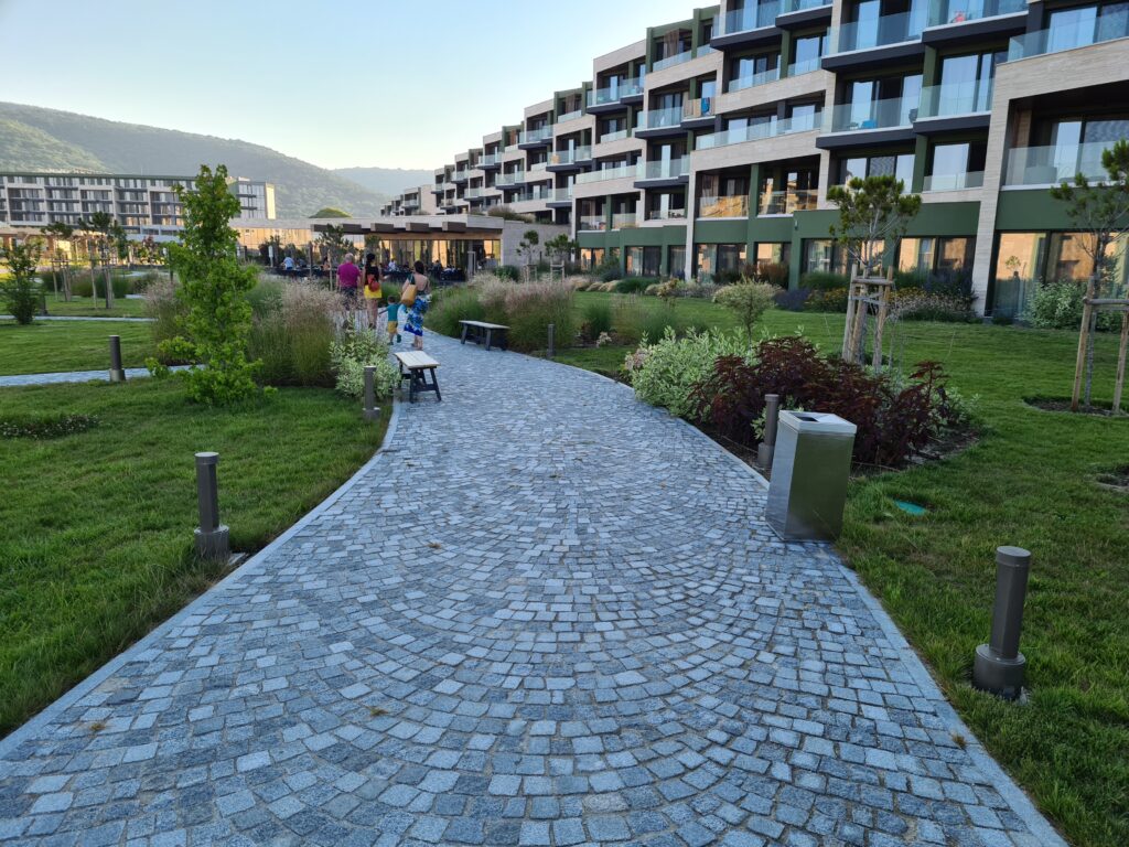 Alee pietruită printre grădini și clădiri hoteliere cu balcoane