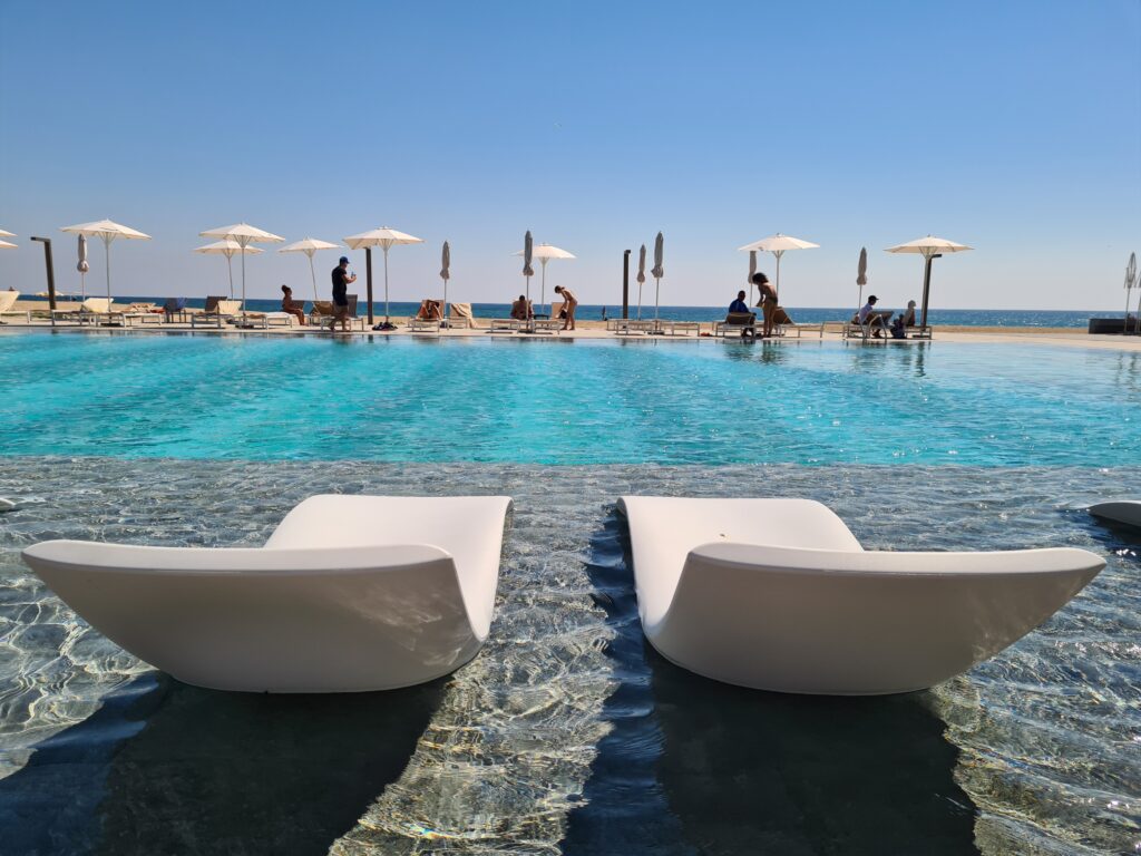 Două șezlonguri albe amplasate în apa puțin adâncă a piscinei