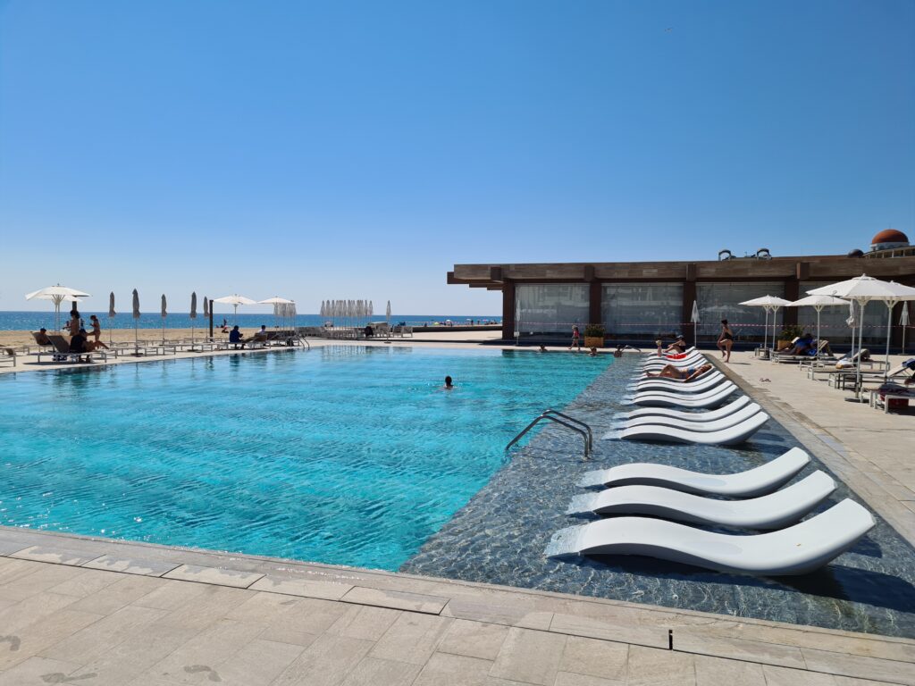 Șir de șezlonguri albe în apă, pe marginea piscinei