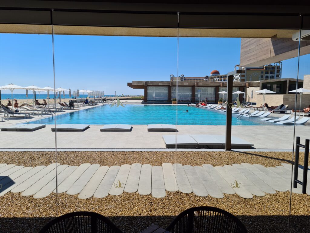 Piscină și șezlonguri văzute prin ferestrele unei terase acoperite