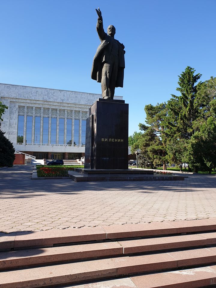 Statuie pe soclu înalt în fața unei clădiri monumentale