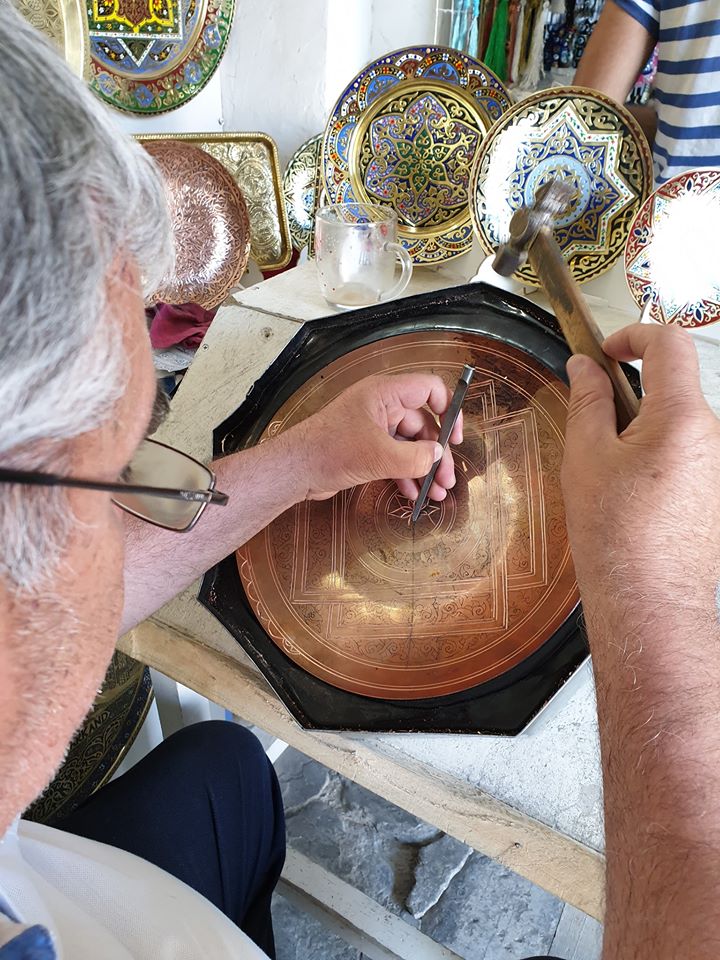 Meșter gravând o farfurie metalică cu unelte de mână