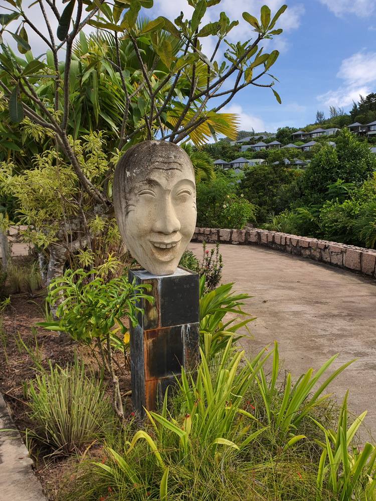 Sculptură reprezentând un chip, amplasată printre plante tropicale