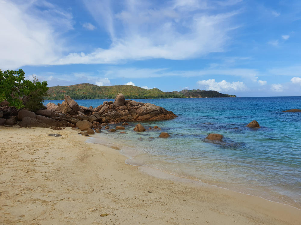 Plajă cu nisip deschis, stânci și mare albastră