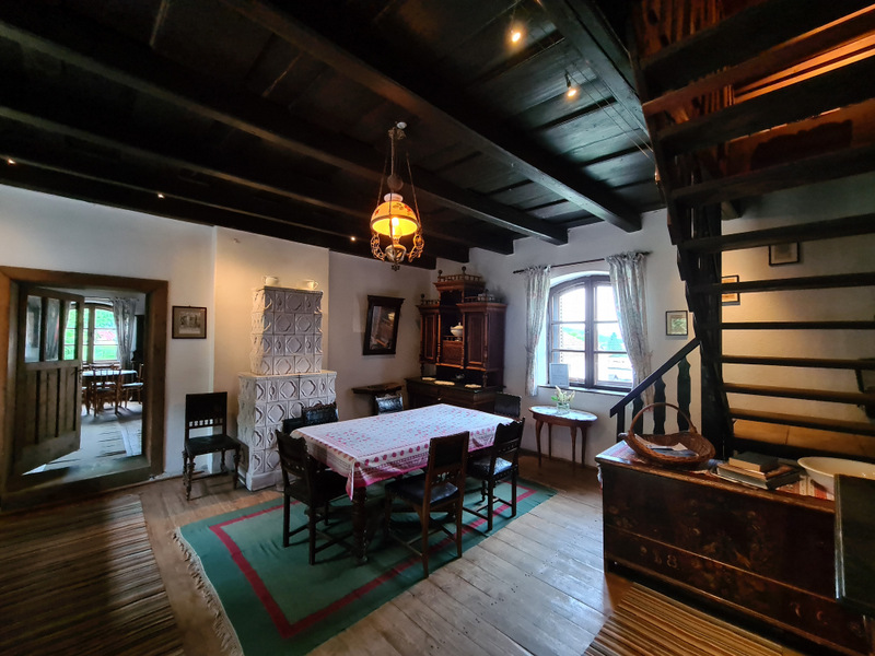 Masă cu scaune din lemn, covor verde și scară într-o cameră rustică
