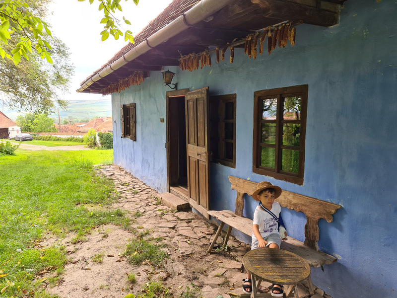 Fațadă albastră cu ferestre din lemn și bancă lângă intrare.