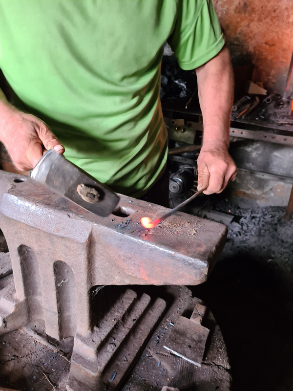 Detaliu cu mâinile unui fierar și metal încins pe nicovală.