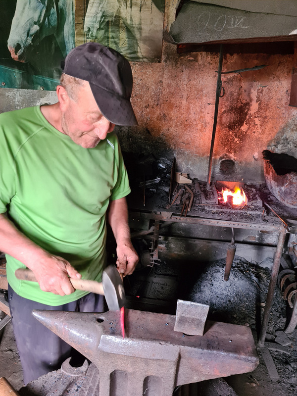 Fierar lucrând cu ciocanul la nicovală, lângă focul din atelier.