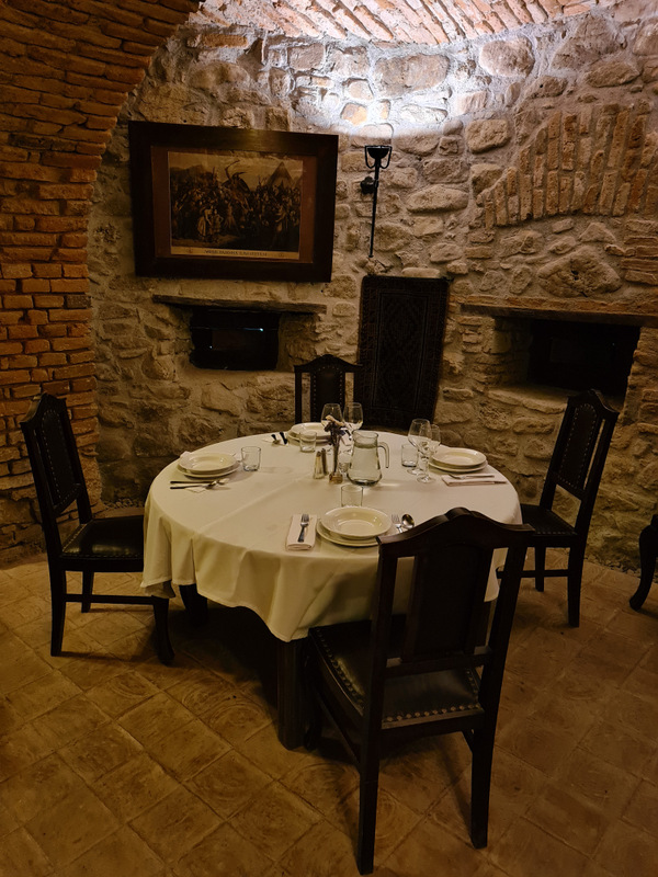 Masă rotundă pregătită pentru cină sub o boltă din cărămidă.