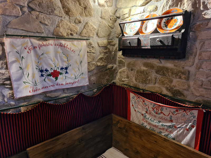Bancă de colț din lemn cu textile brodate și farfurii decorative.