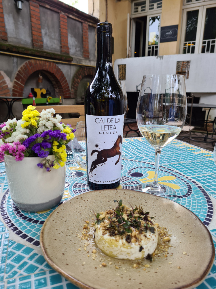 Preparat pe farfurie alături de sticlă de vin și pahare, pe terasa unui restaurant.