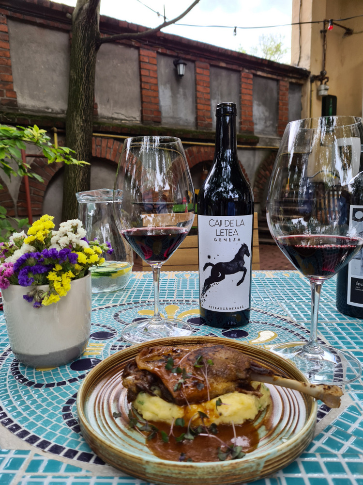 Farfurie cu preparat gătit și pahare de vin pe masa unei terase.