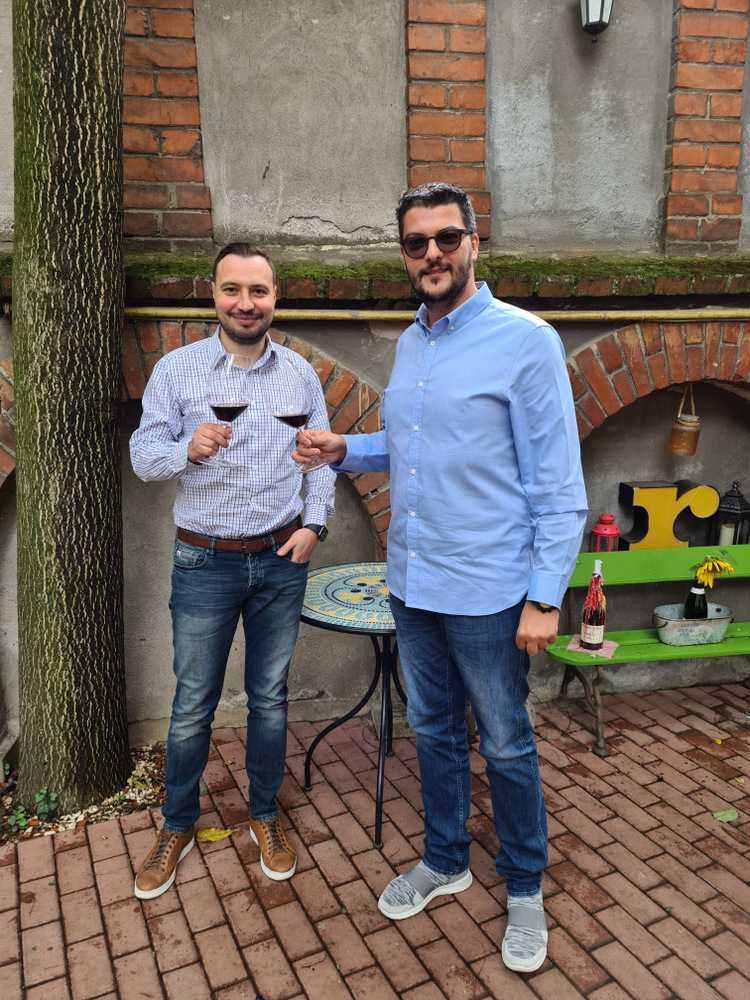 Doi bărbați cu pahare de vin în fața unei clădiri vechi.