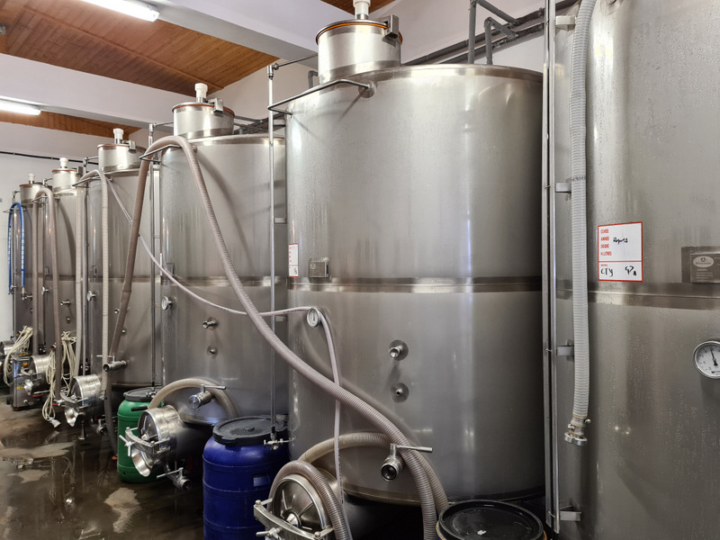Rezervoare mari din inox și furtunuri într-o hală de producție.
