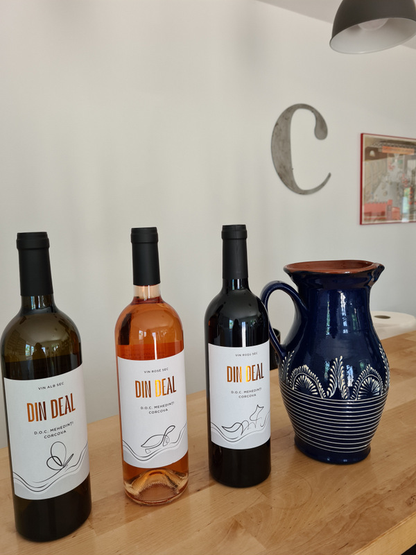 Trei sticle de vin și o carafă ceramică albastră pe masă.
