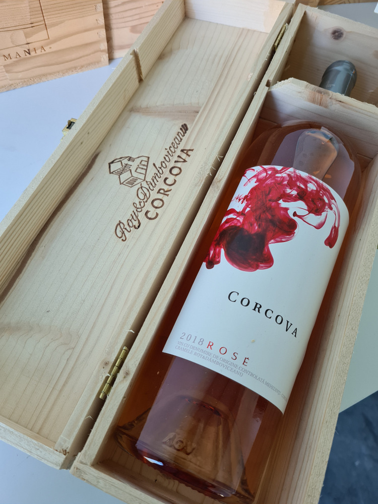 Sticlă de vin roze într-o cutie de lemn cu capac inscripționat.