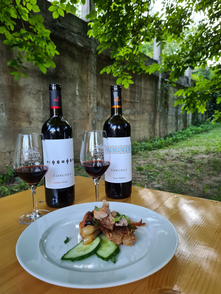 Sticle și pahare de vin lângă farfurie cu carne și legume.