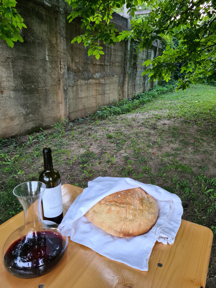 Pâine rotundă pe un șervet alb lângă sticlă și pahar de vin.