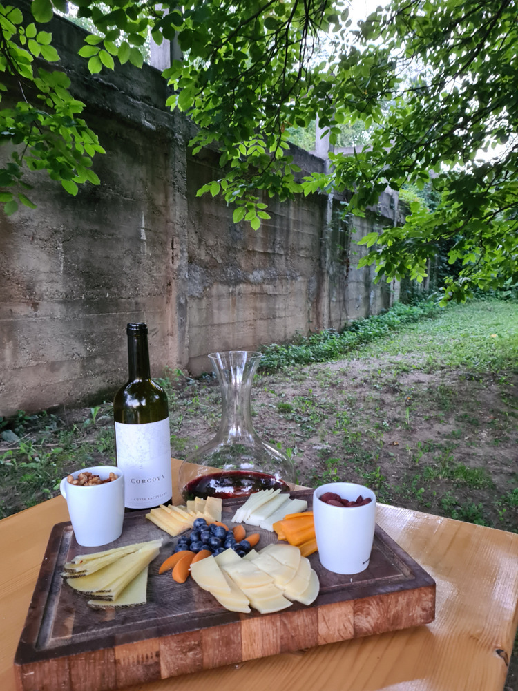 Platou cu brânzeturi, fructe și cești lângă o sticlă de vin.
