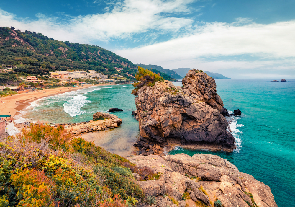 Stânci și vegetație de coastă lângă o plajă cu valuri