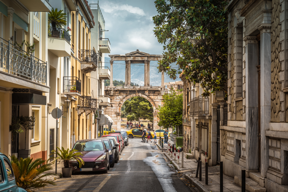 Stradă urbană cu clădiri neoclasice și ruine cu coloane în capăt.