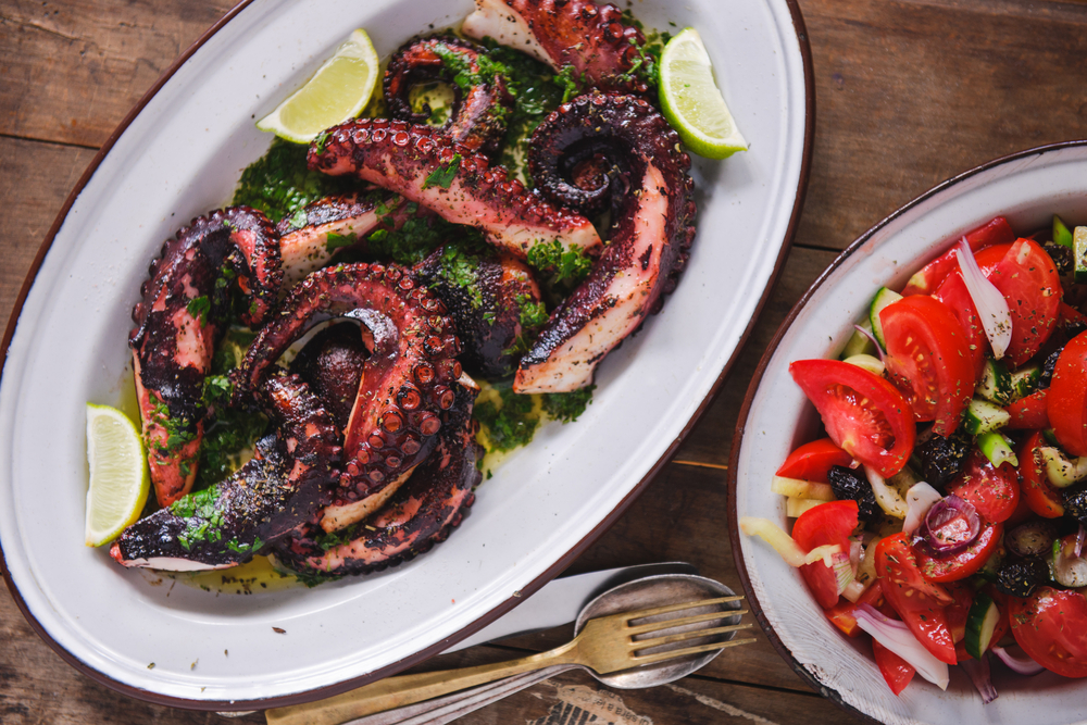 Tentacule de caracatiță la grătar cu lime, lângă salată de roșii.
