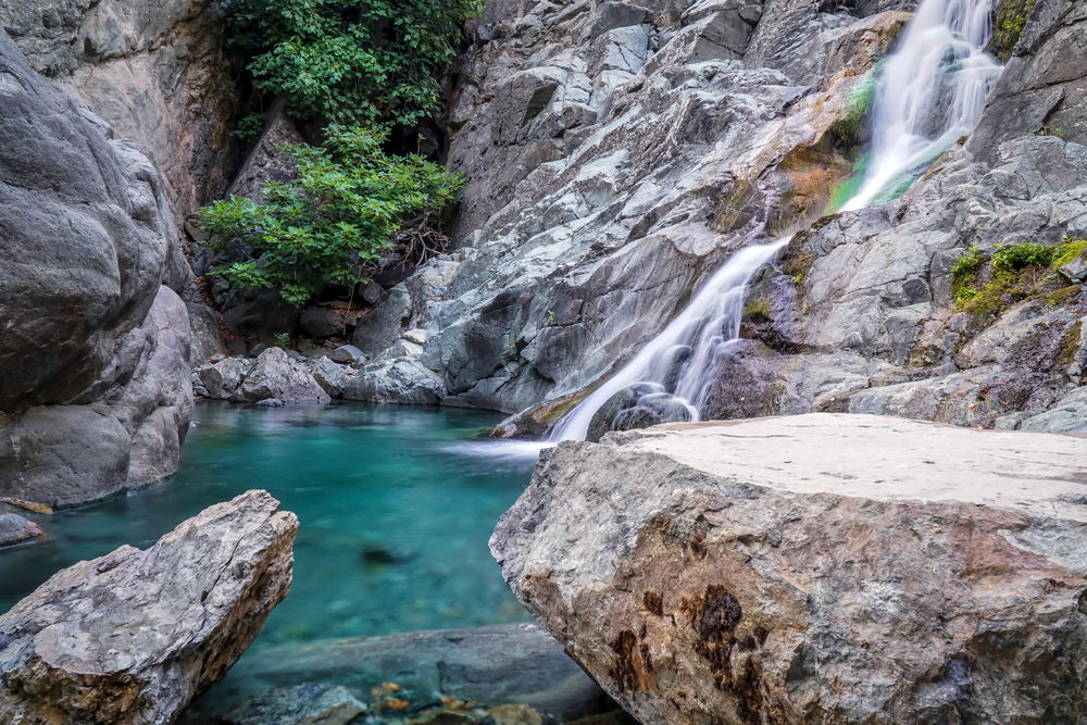 Cascadă printre stânci, deasupra unui bazin natural cu apă turcoaz.