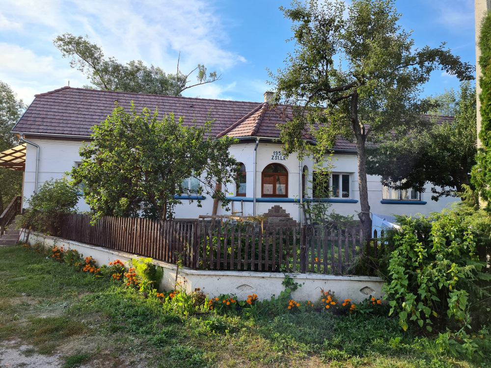 Casă albă cu acoperiș înclinat și grădină cu flori