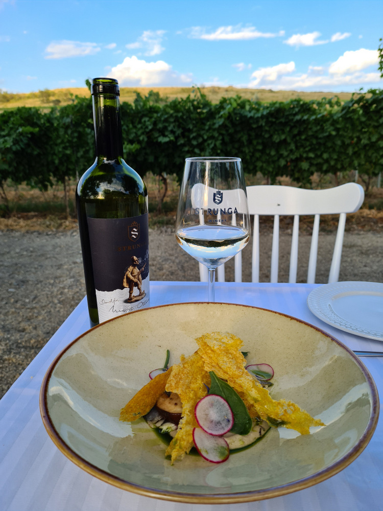 Farfurie cu preparat decorat, lângă o sticlă de vin