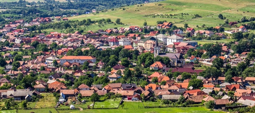 Localitate cu acoperișuri roșii, între dealuri verzi