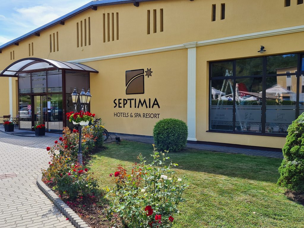 Intrare într-o clădire galbenă, lângă o grădină cu flori.