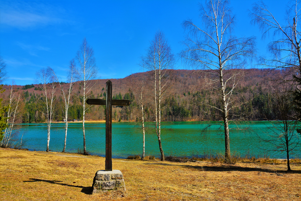 Cruce din lemn lângă un lac turcoaz și pădure