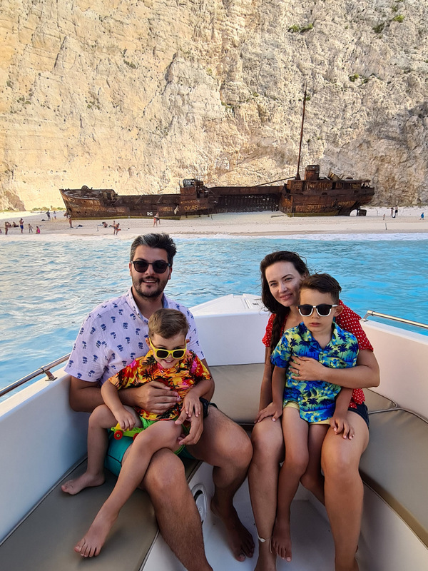 Familie așezată într-o barcă, cu epavă și stânci în fundal