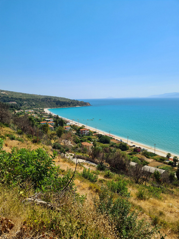 Plajă lungă și mare albastră văzute de pe un versant verde