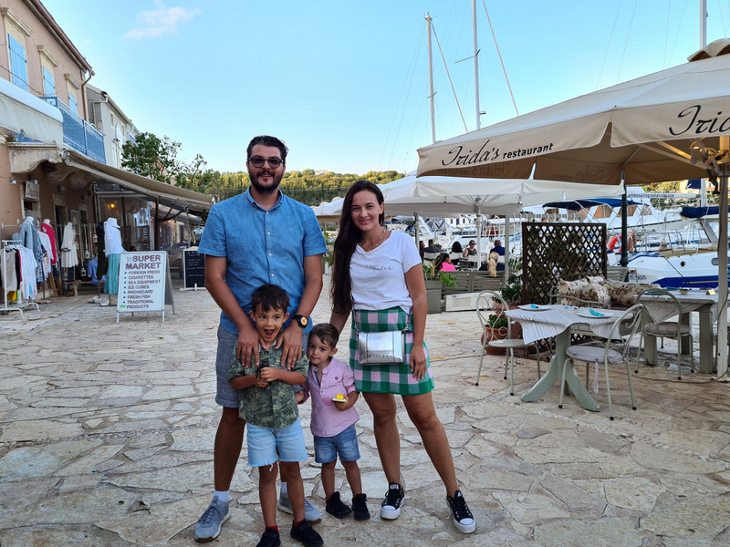 Familie pozând pe o promenadă cu restaurante și bărci în fundal