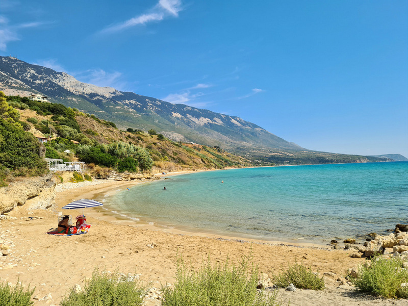 Plajă cu nisip și mare calmă la poalele munților