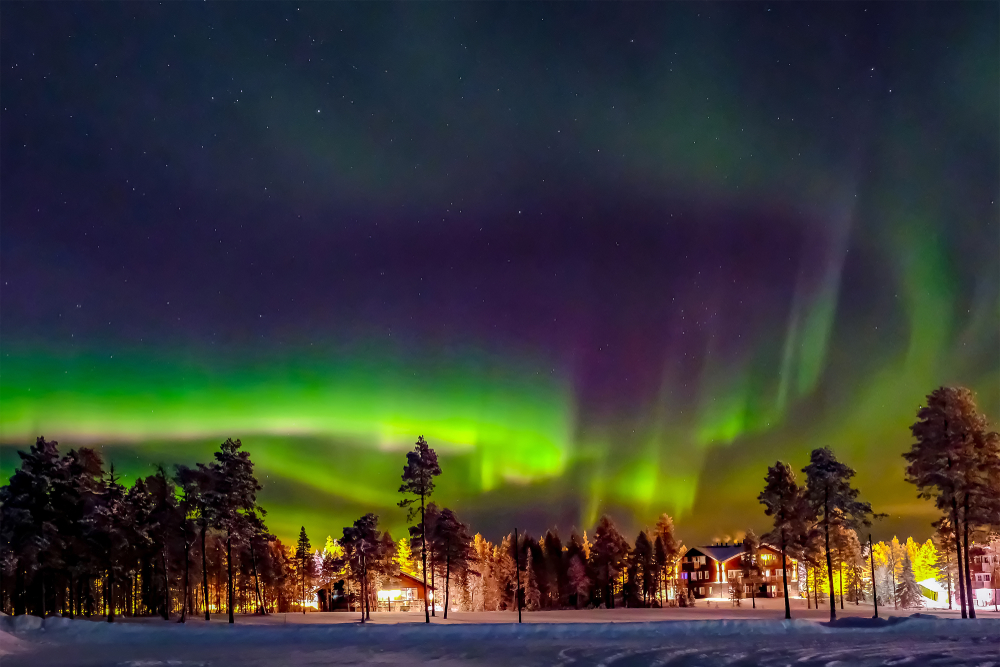 Auroră verde și violetă, deasupra unui peisaj înzăpezit