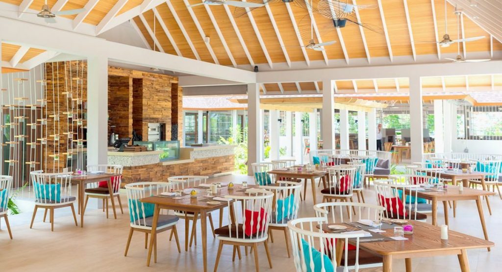 Restaurant lumineux avec tables, chaises et charpente apparente en bois.