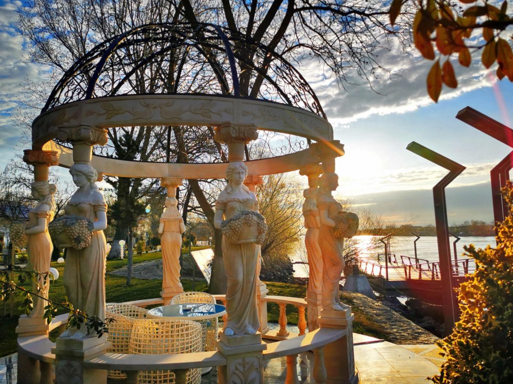 Foișor circular cu coloane sculptate, lângă apă.