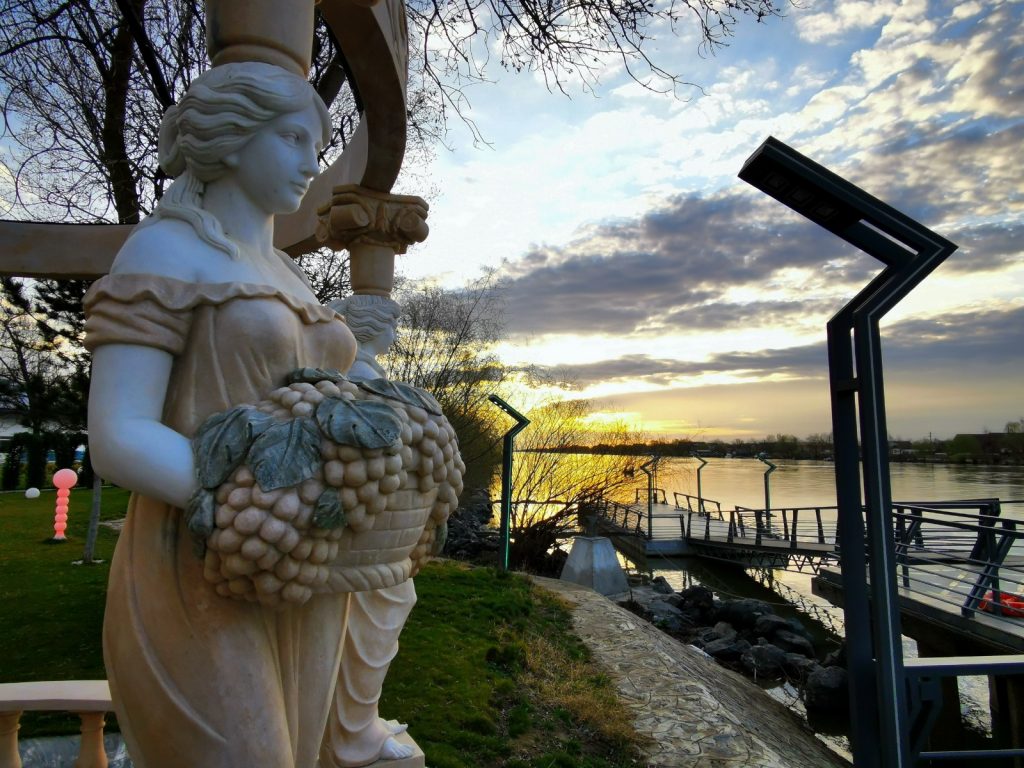 Statuie feminină lângă apă, în lumina apusului.