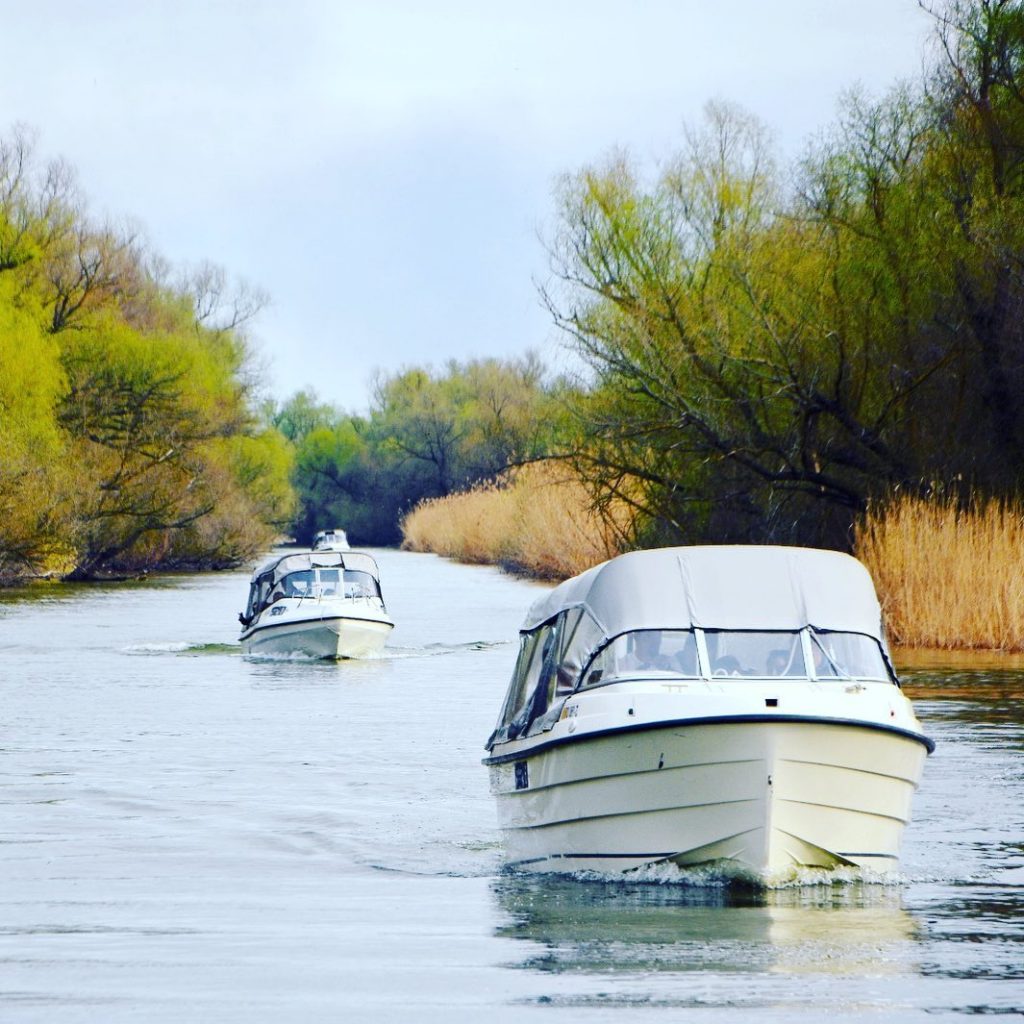 Două bărci cu motor pe un canal mărginit de arbori.