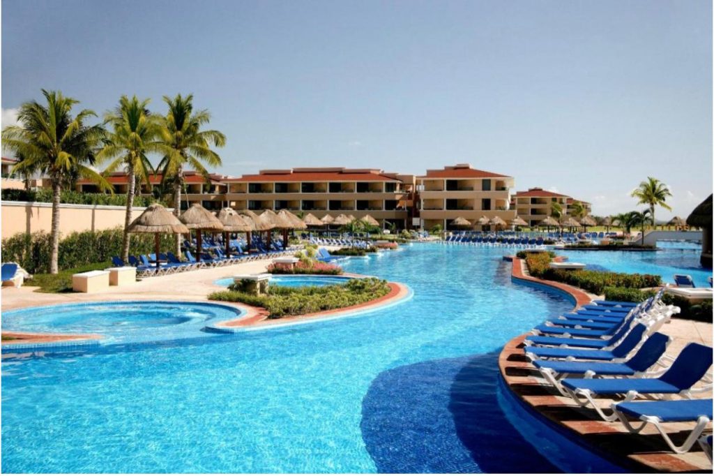 Piscină cu apă albastră, șezlonguri și palmieri în jur.