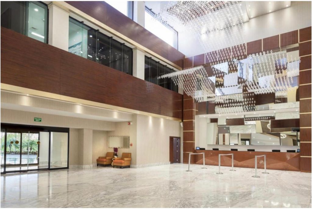 Hol înalt cu balustrade, pereți vitrați și decor geometric suspendat.