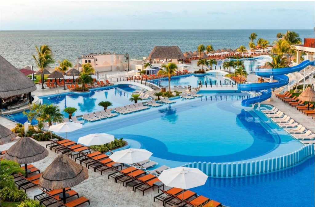 Piscine și zone de relaxare cu umbrele, într-un complex cu palmieri.