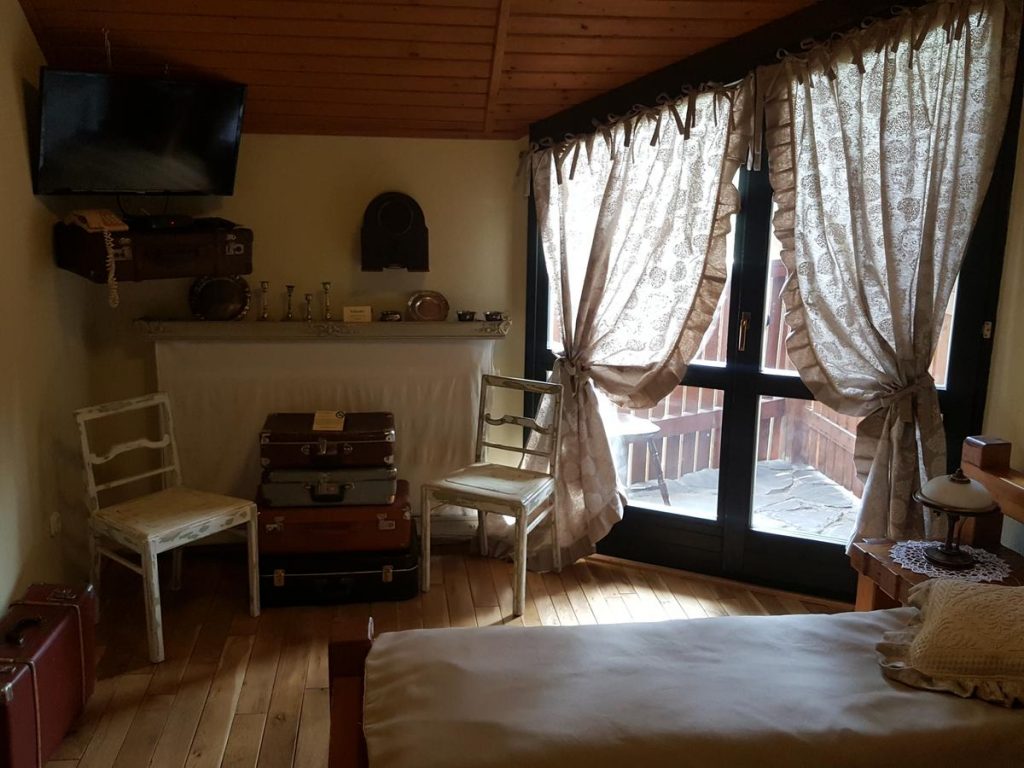 Salon rustic cu sobă, fotolii și ferestre acoperite cu perdele.