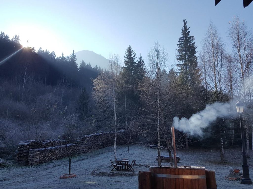 Ciubăr aburind într-o curte înzăpezită, înconjurată de arbori.
