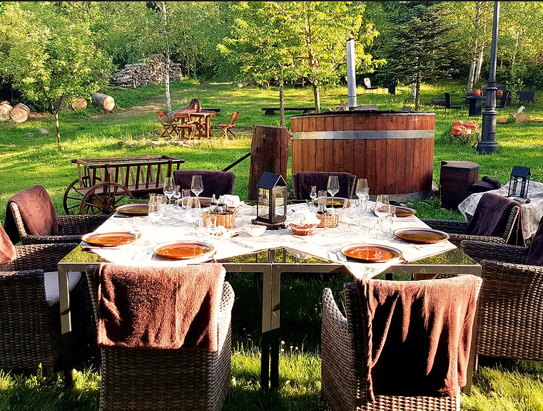 Masă pregătită în grădină, lângă un ciubăr din lemn.