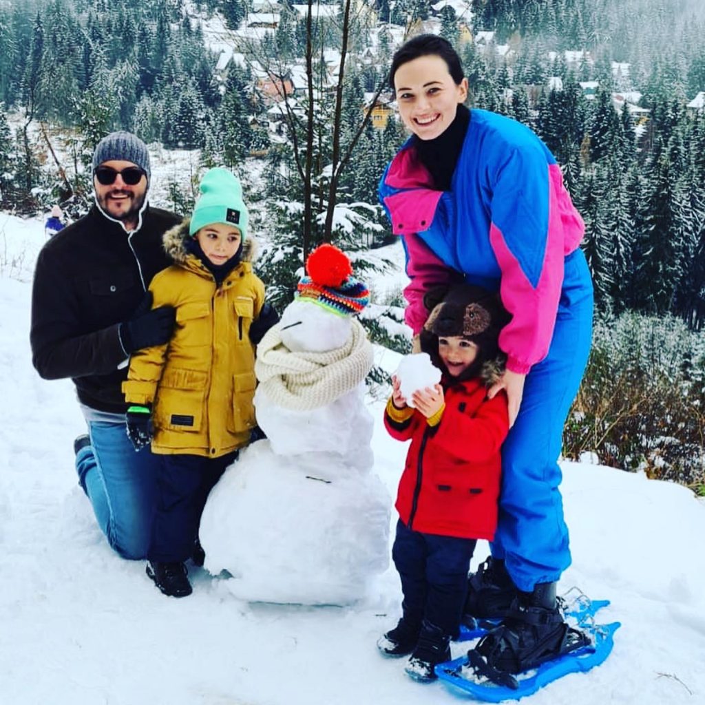 Familie lângă un om de zăpadă între brazi